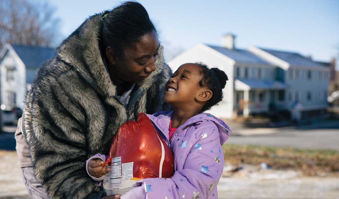 Mother looking adn hugging her young daughter who is holding big frozen turkey