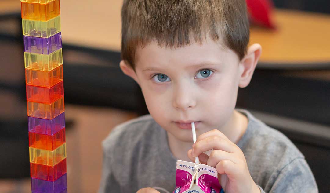 A little boy sipping on a small carton of milk